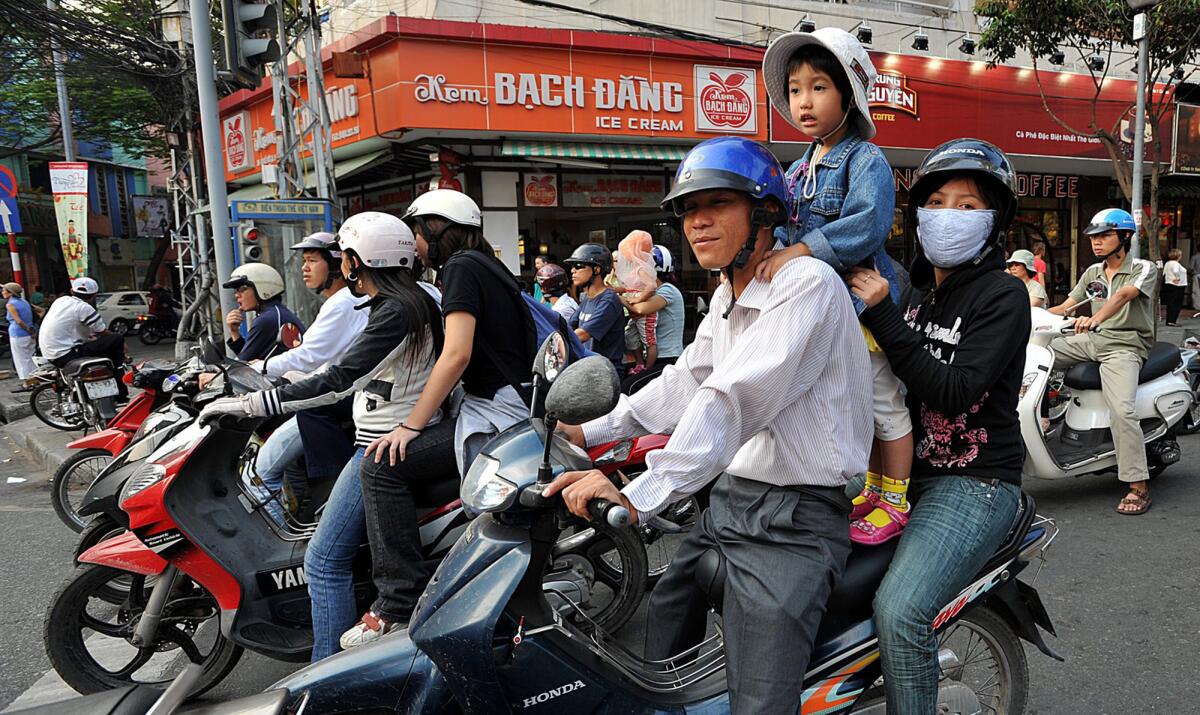 Motor scooter riders, most wearing helmets, compete for space in Ho Chi Minh City, which has about 6 million residents.