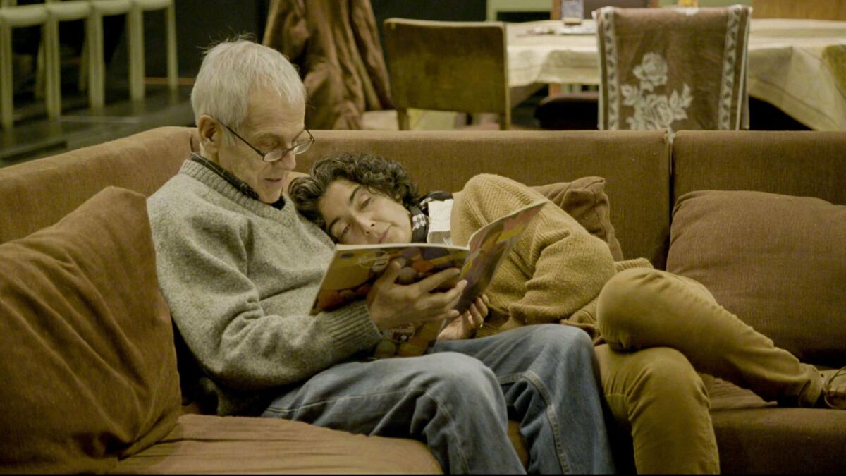 An elderly couple sits together on their couch.