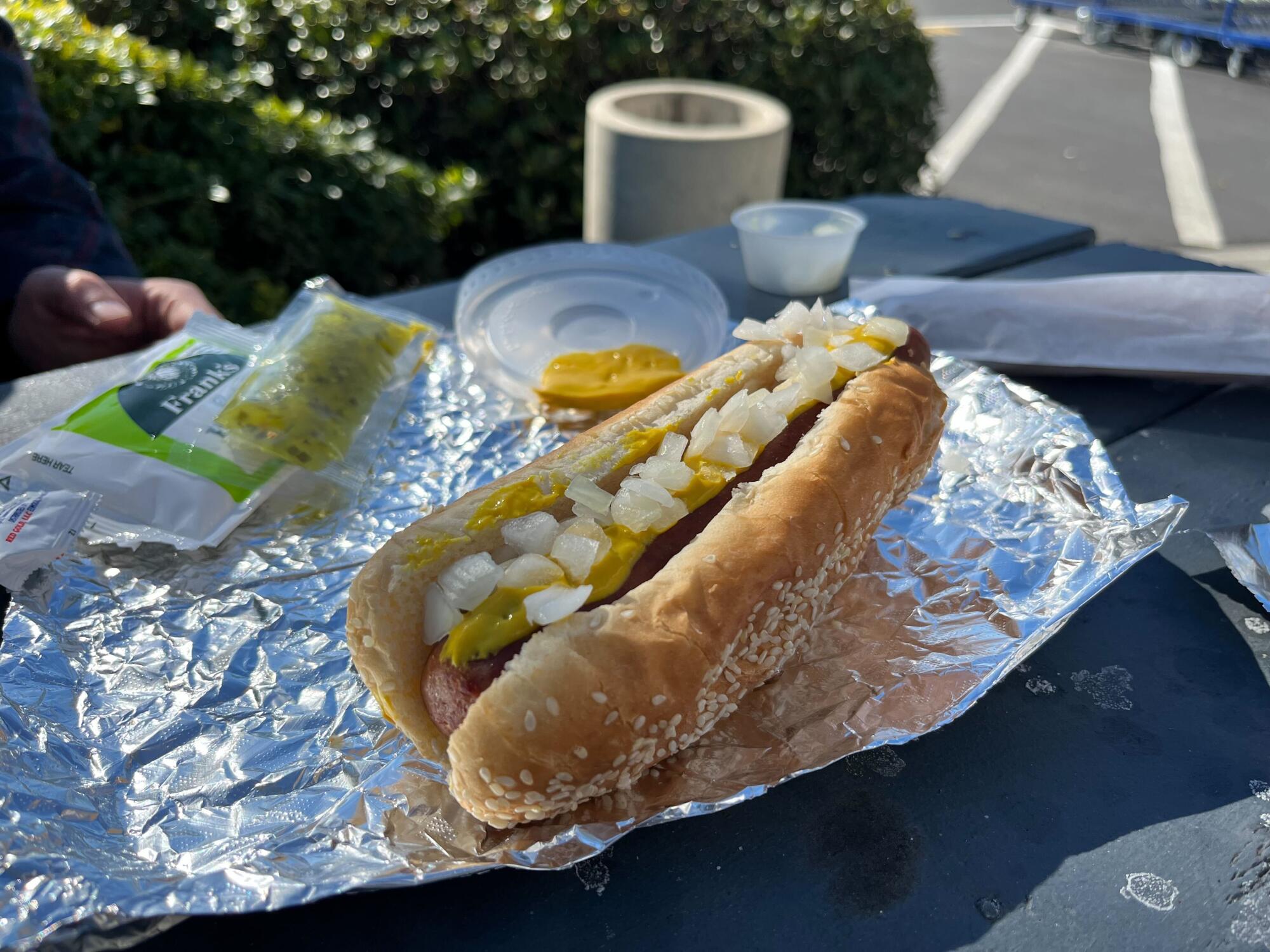 Hot dog with mustard and onion on top of it on foil wrapping outside 