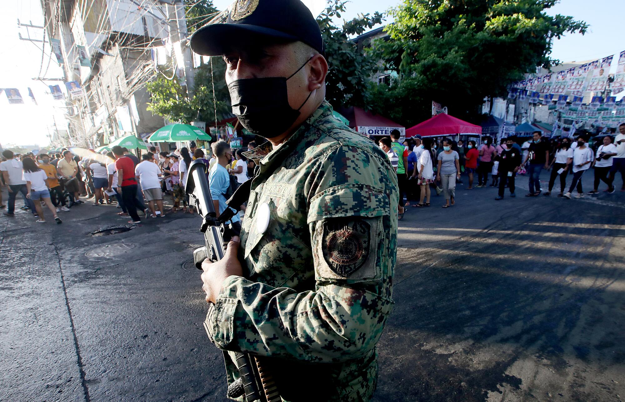 A Philippine National Police officer stands guard as people line up to vote in a neighborhood in the Port of Manila.