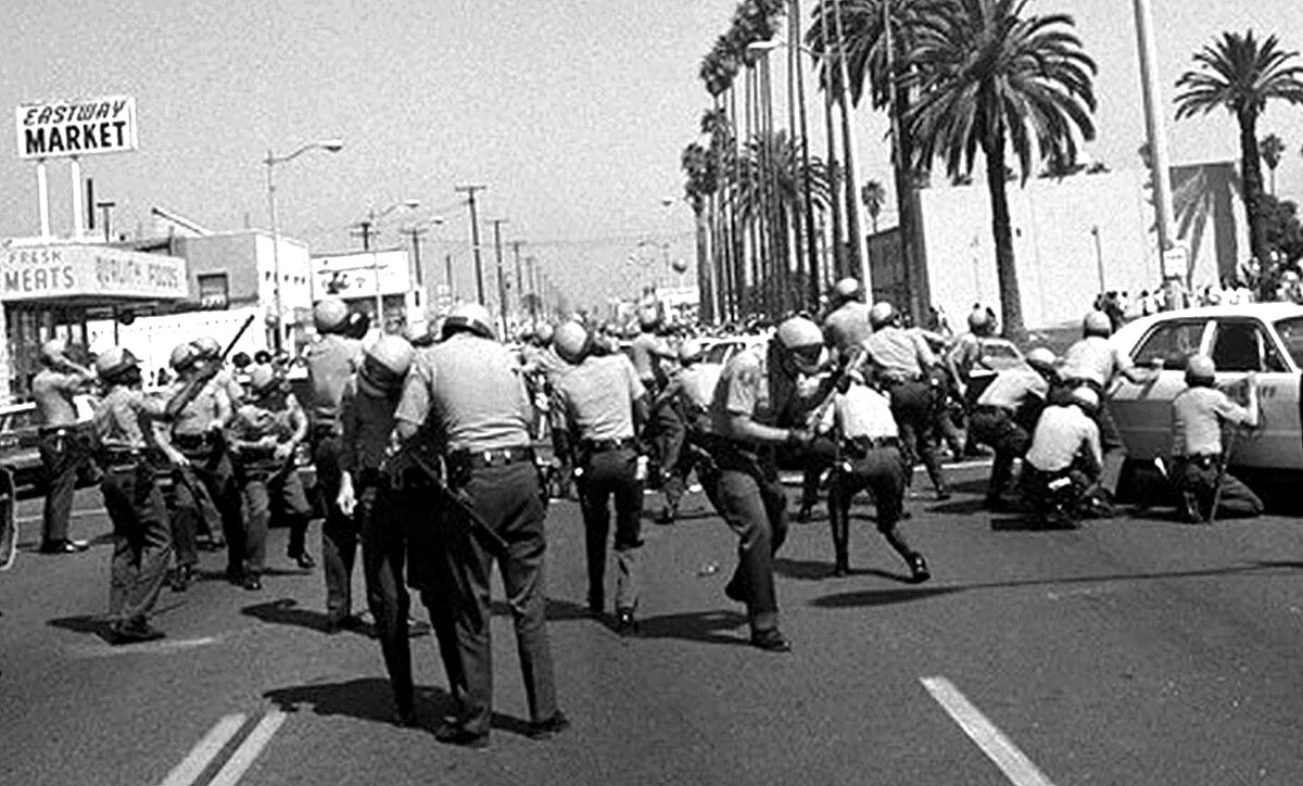 Sheriff's deputies duck behind cars on Whittier Blvd. to avoid rocks and bottles during the Chicano Moratorium in 1970