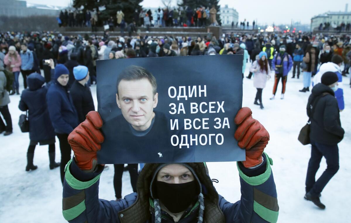 A man, surrounded by protesters in a snowy square, holds a poster with a portrait Alexei Navalny.