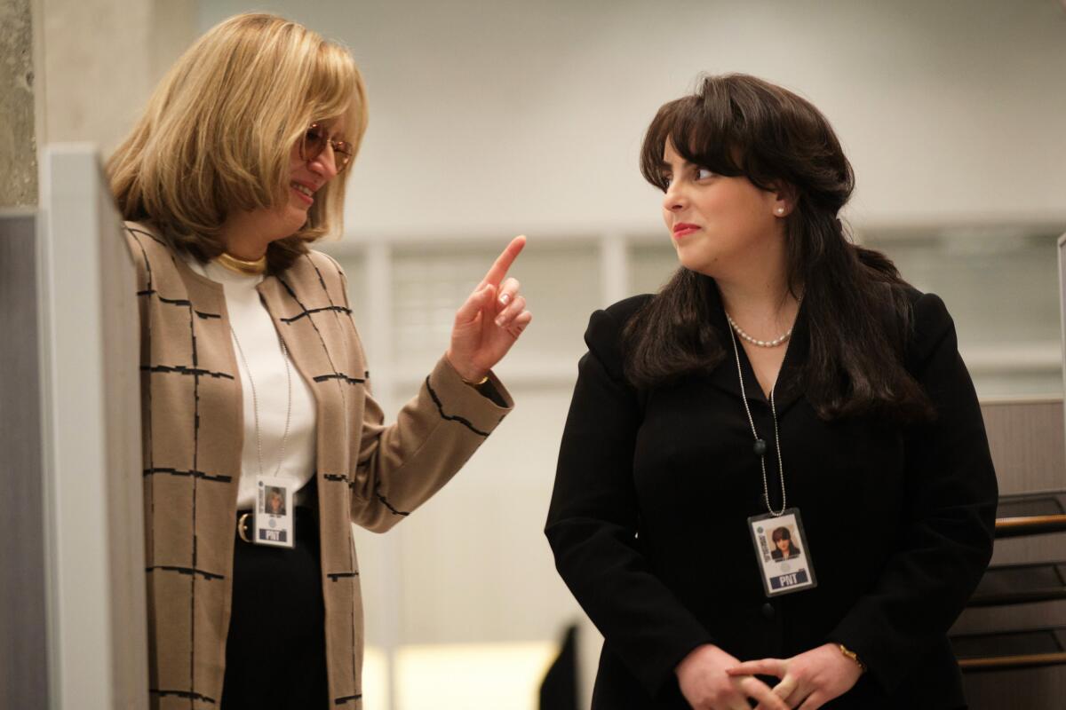 Two women talk amid office cubicles.