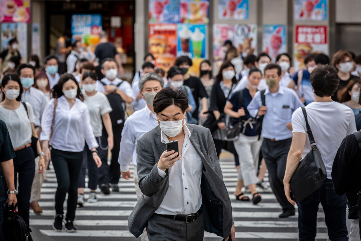 A man wearing a face mask in a crowd of masked people crosses a street 