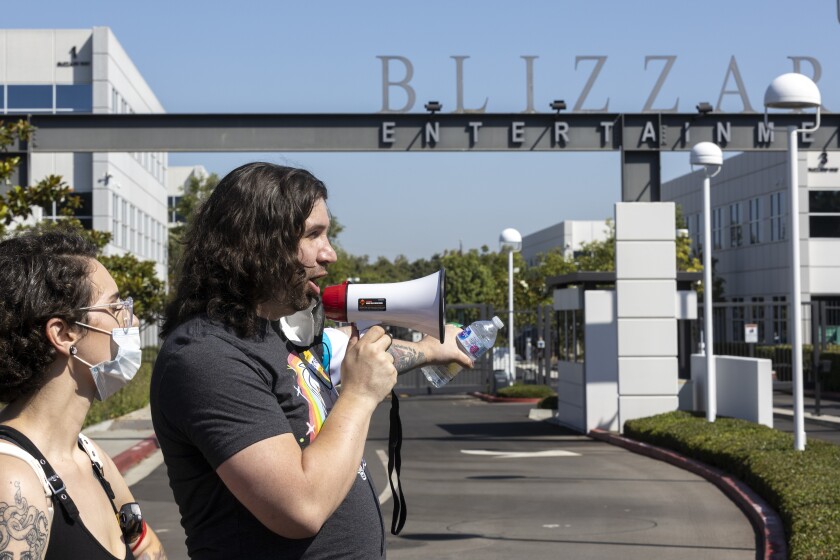 A man standing beside a woman holds a megaphone in front of the Activision Blizzard building in Irvine.