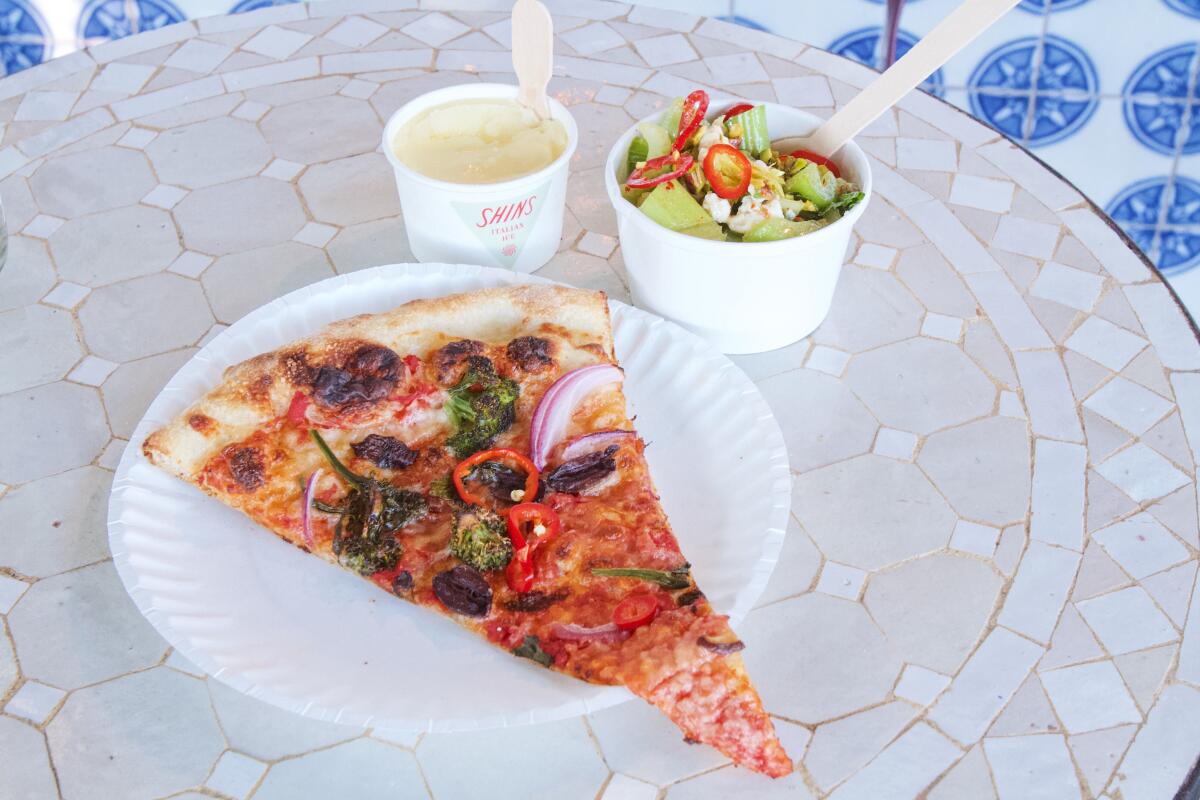 A slice of vegetarian pizza, a cup of celery salad and an Italian ice on a tiled table at Shins Pizza in Cypress Park.