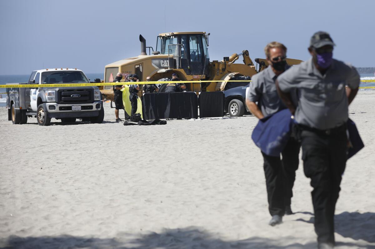 A tractor, truck and caution tape on a beach. Two people carry a gurney 