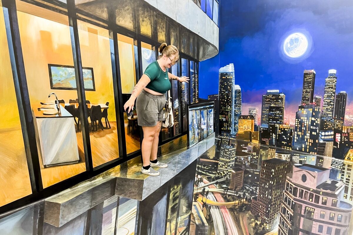 A woman stands above an optical illusion of a city street