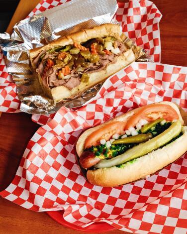 An Italian beef sandwich behind a Chicago dog at Juicy J's in Koreatown, each atop checkered red and white paper