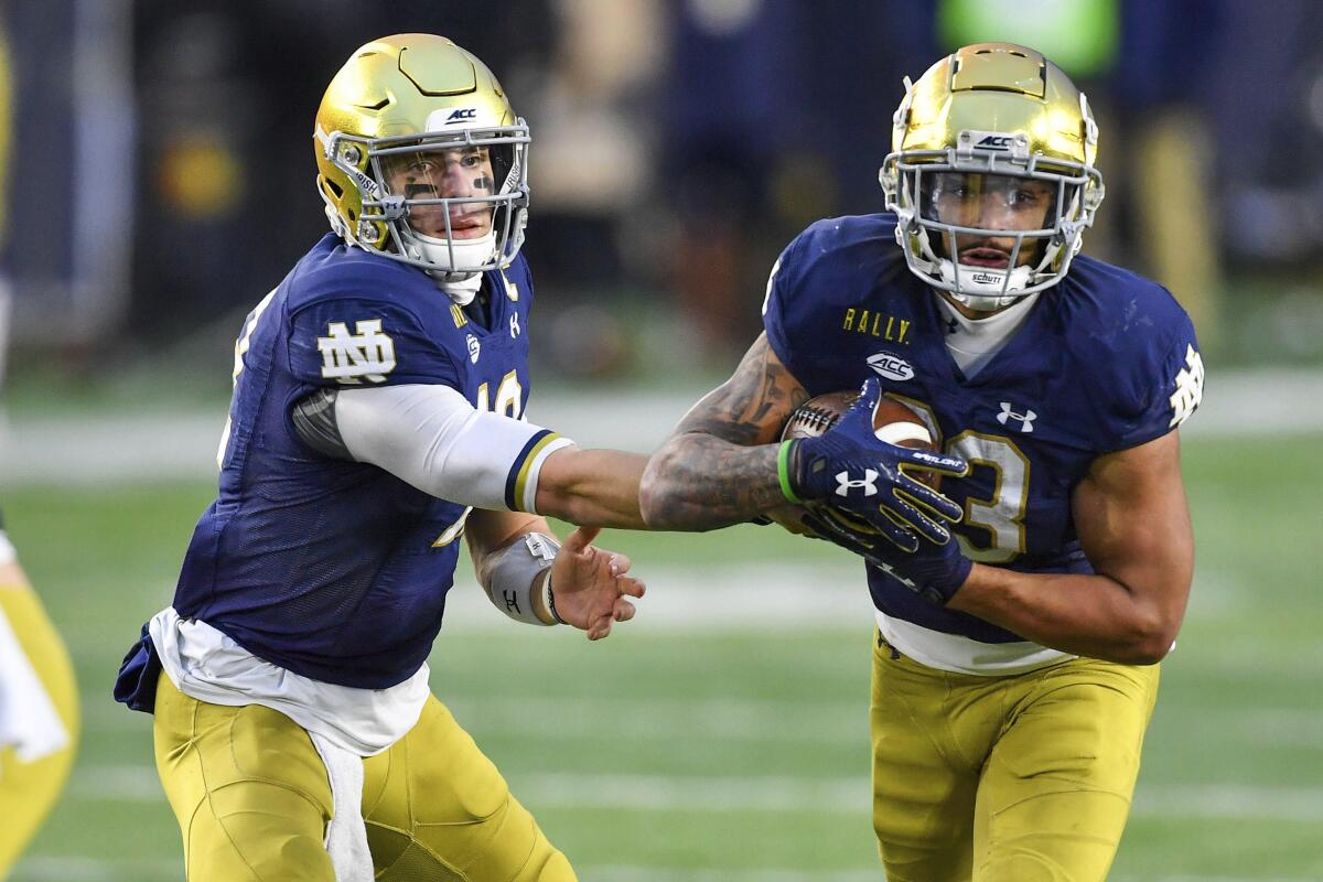 Notre Dame quarterback Ian Book (12) hands off to running back Kyren Williams (23) during the third quartero of the team's NCAA college football game against Syracuse on Saturday, Dec. 5, 2020, in South Bend, Ind. (Matt Cashore/Pool Photo via AP)