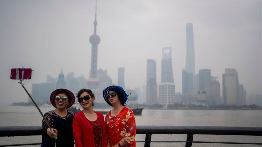 Three women take a selfie at the promenade on the Bund along the Huangpu River in Shanghai. An Air China fare of $425 for late summer until mid-October puts the city within reach.