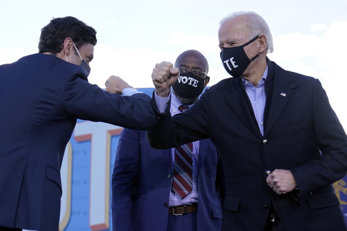 President-elect Biden elbow-bumps one Democratic Senate candidate, Jon Ossoff, as another, Raphael Warnock, looks on Monday.