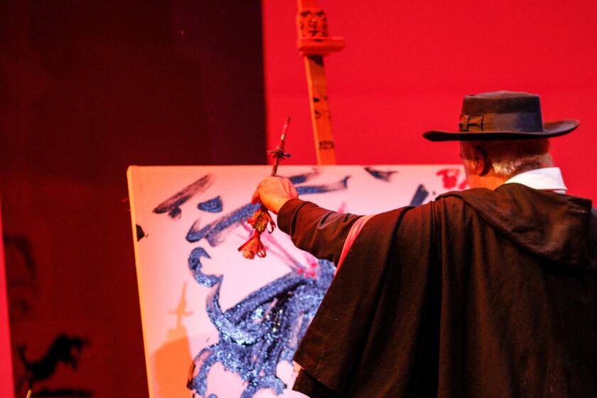 An actor in a hat and cape on stage painting on a canvas