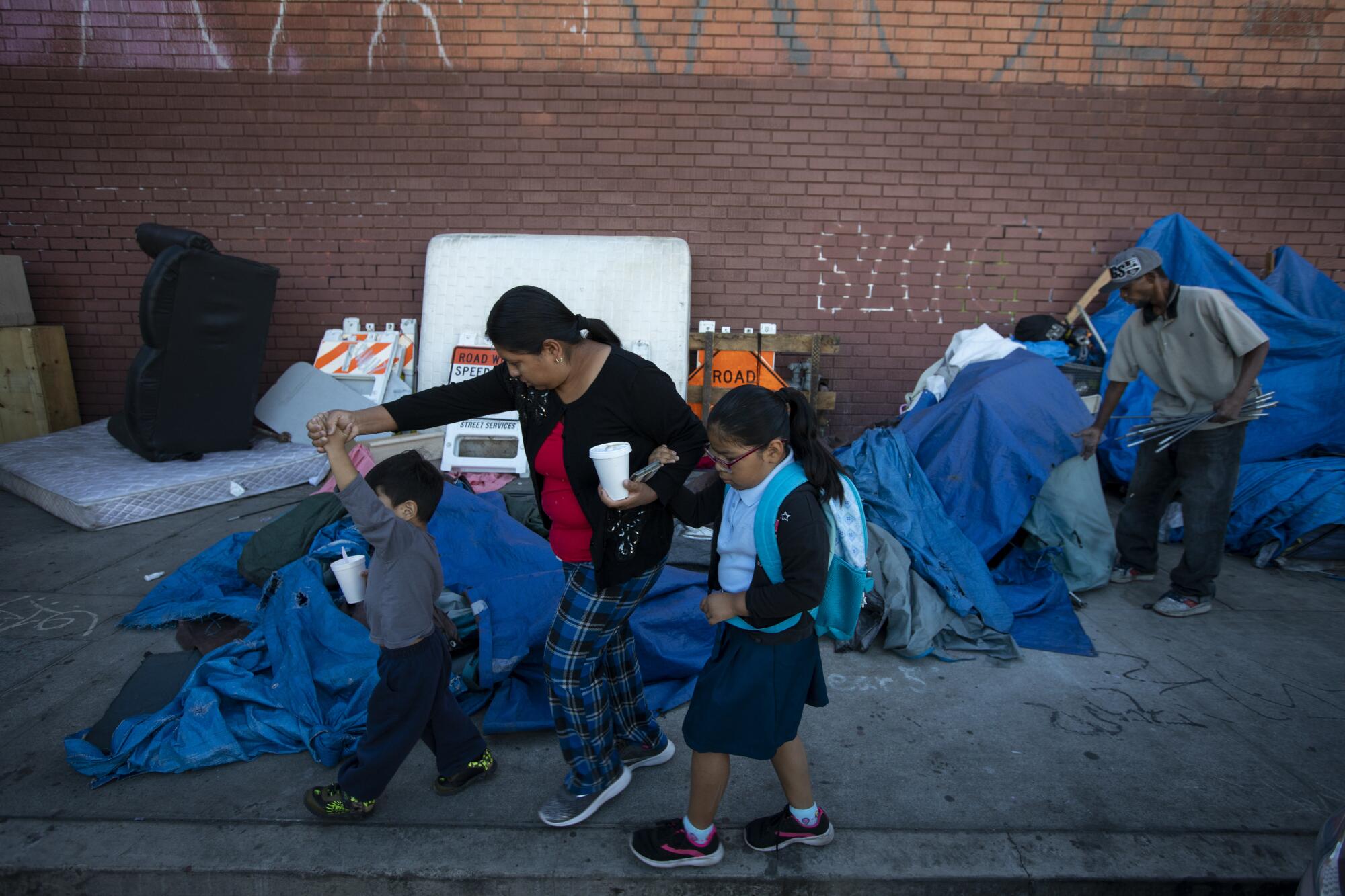 A mother walks her children past an encampment on Main Street in Los Angeles.