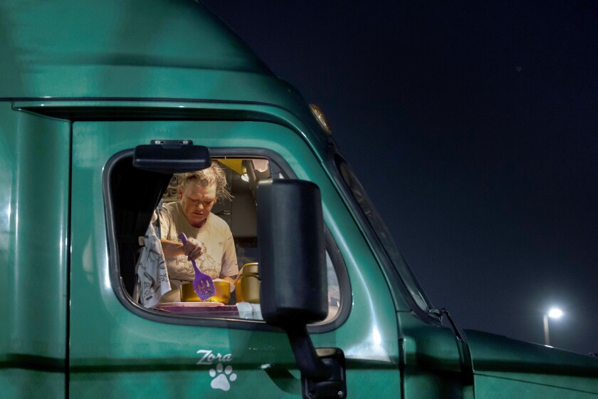 A woman plates her meal that she prepared on a portable induction cooktop and air fryer in the cabin of her truck.