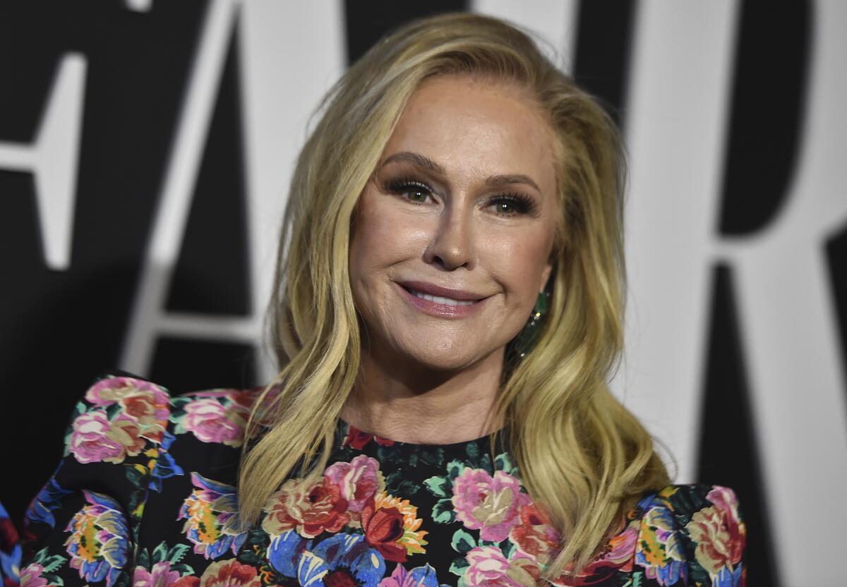 A blond woman wearing a black dress with floral print smiles for photos