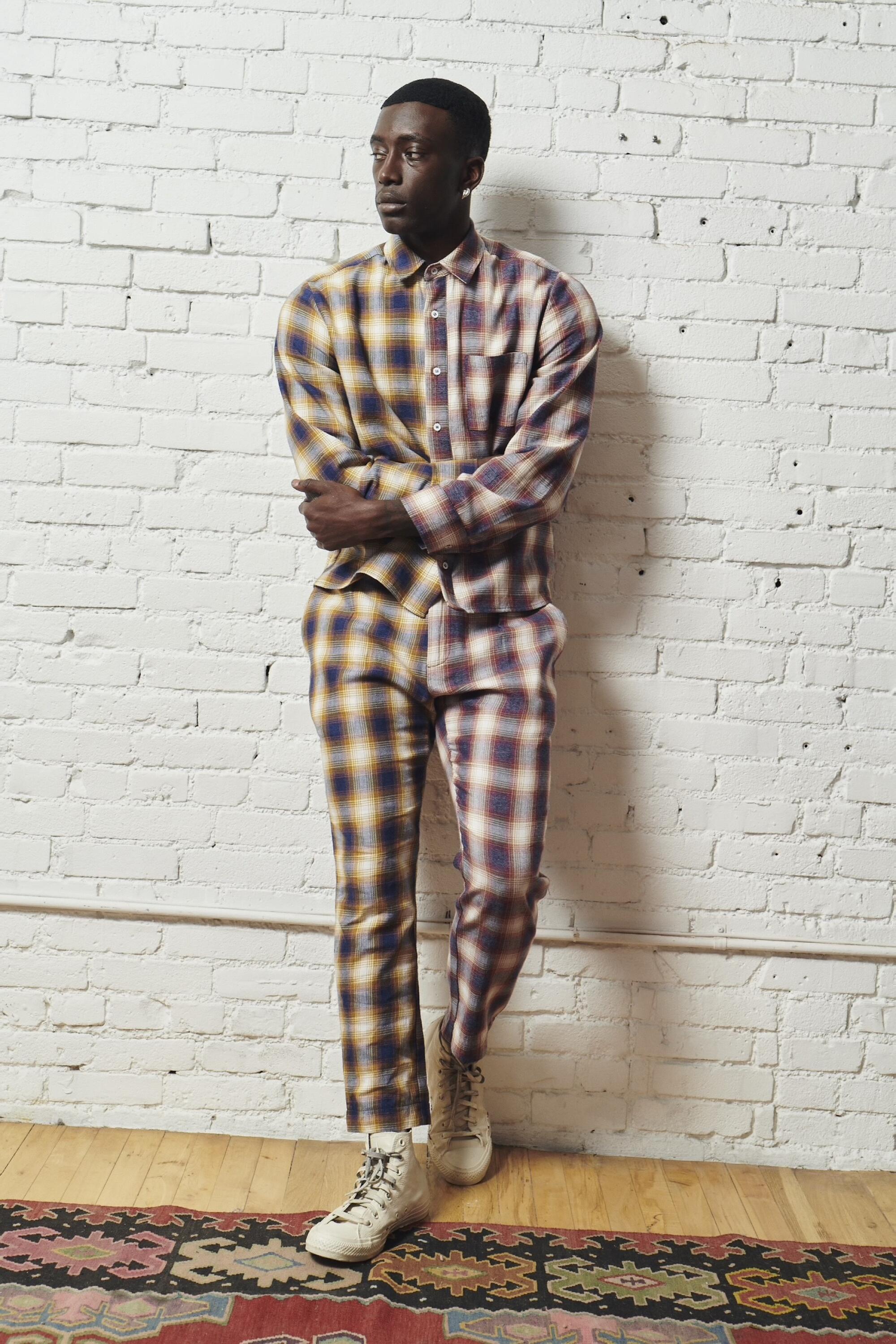 A man dressed head to toe in checked flannel leans against a wall.