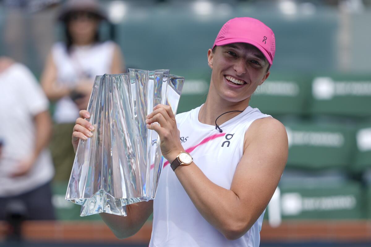 IA woman wearing a pink sports hat poses with a trophy
