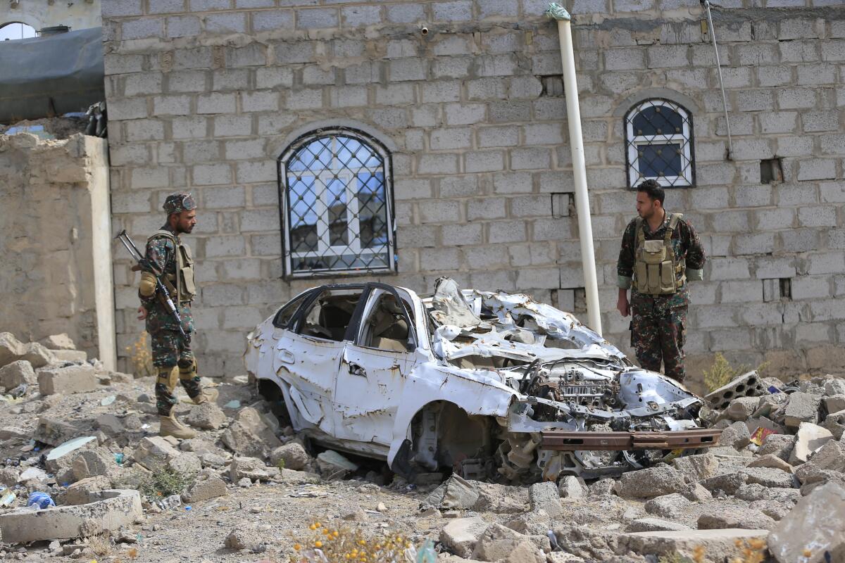 Yemeni soldiers stand over rubble of a building and car.