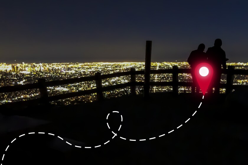 Two people and a low fence are shaded in the glow of city lights scattered in the background.