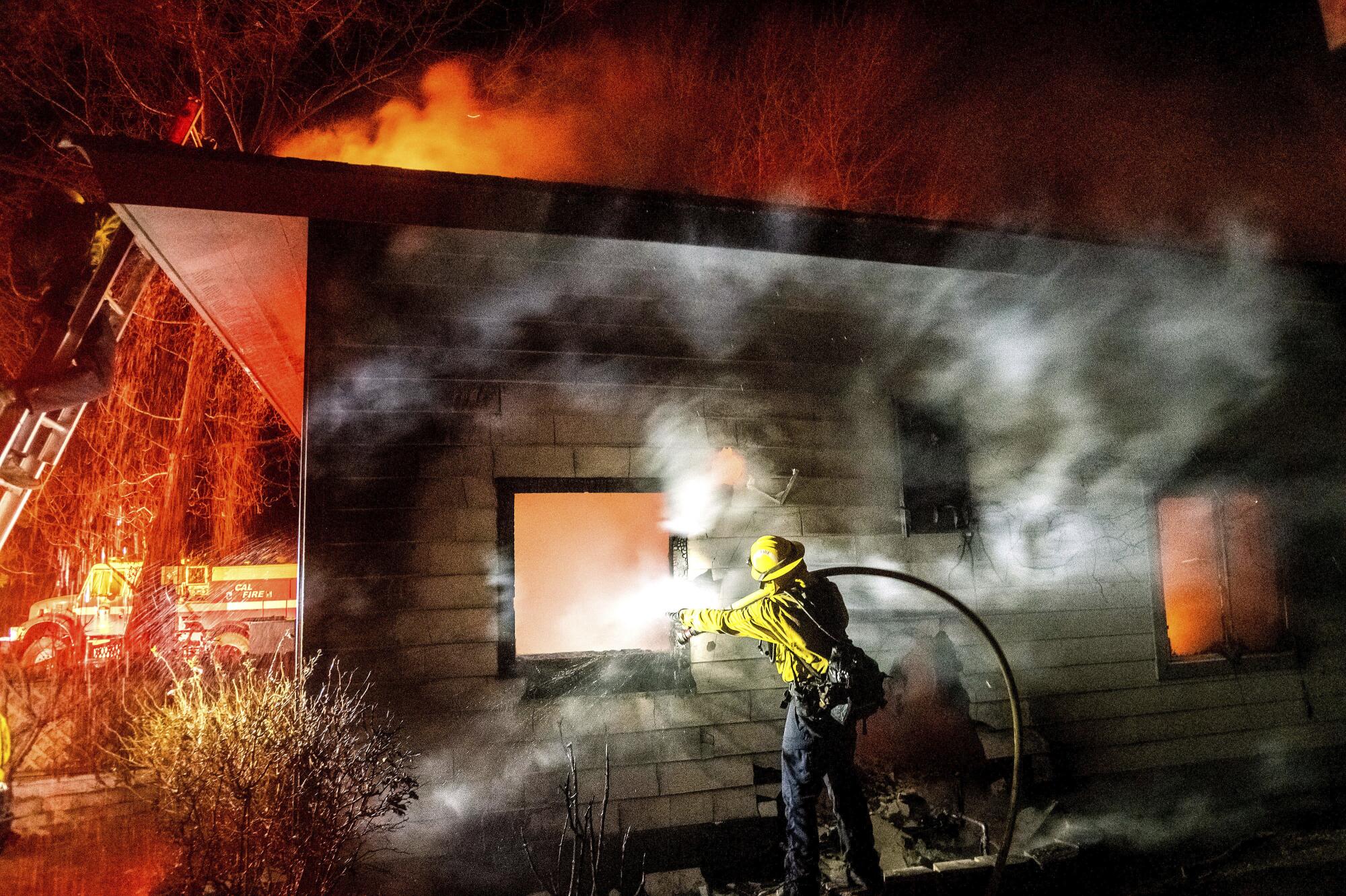 A firefighter holds a hose over his shoulder spraying water at a home