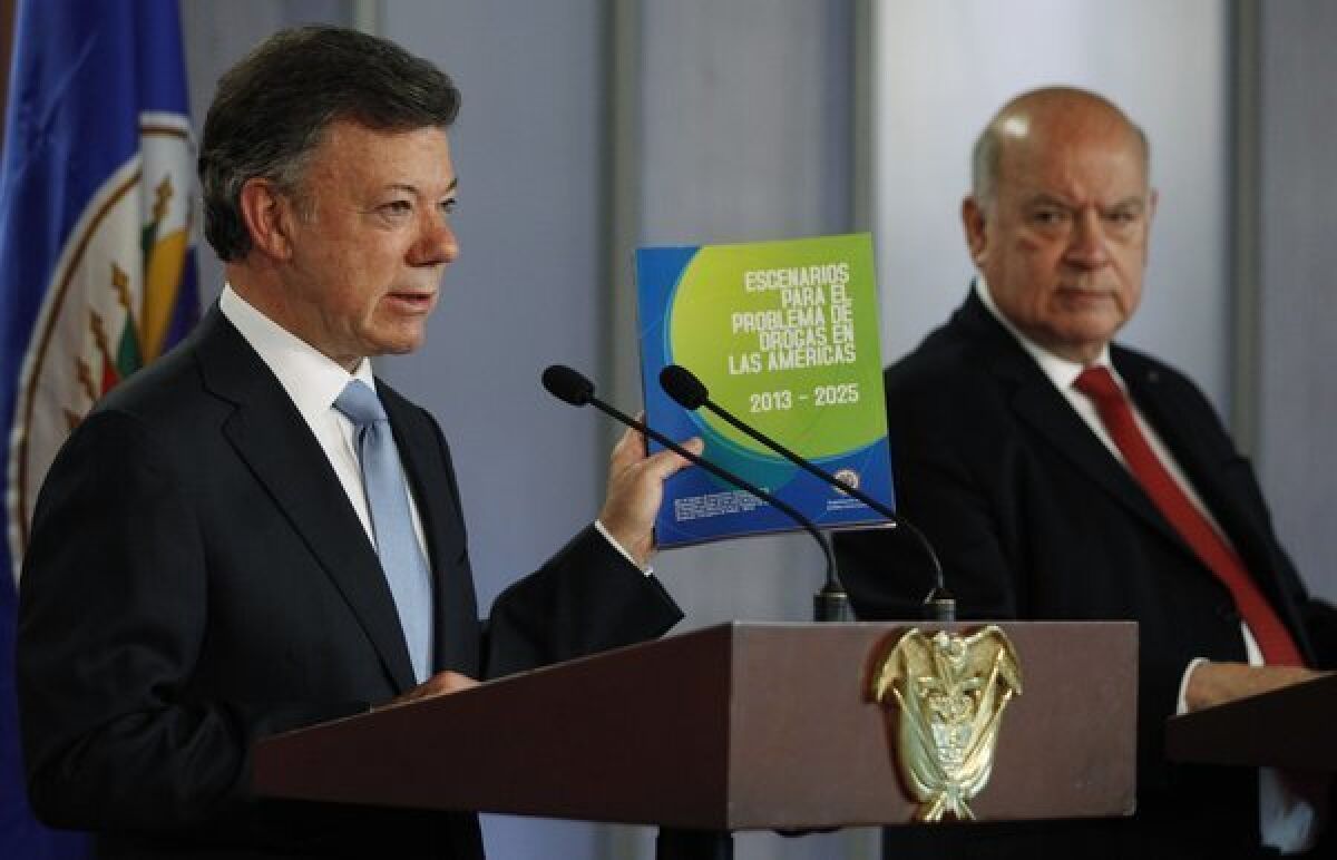 Colombian President Juan Manuel Santos, left, holds a copy of a study on the illicit drug trade presented by Organization of American States Secretary-General Jose Miguel Insulza, right, during a news conference in Bogota, Colombia.