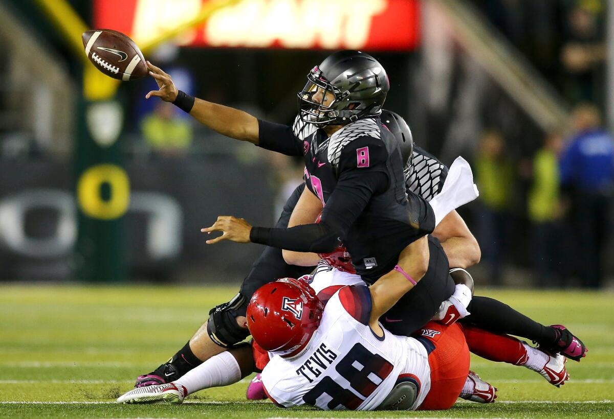 Oregon quarterback Marcus Mariota pitches the ball away while being tackles by Arizona's Jared Tevis on Oct. 2 at Autzen Stadium.