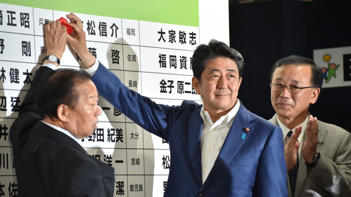 Japanese Prime Minister and ruling Liberal Democratic Party President Shinzo Abe, center, places a rosette on an LDP candidate's name to indicate an election victory in Tokyo on July 10, 2016.