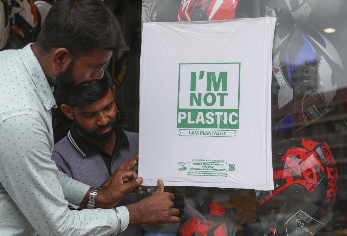 Workers of a helmet store paste degradable plastic substitute material on a glass in Hyderabad, India, Thursday, June 30, 2022. India banned some single-use or disposable plastic products Friday as a part of a longer federal plan to phase out the ubiquitous material in the nation of nearly 1.4 billion people. (AP Photo/Mahesh Kumar A.)