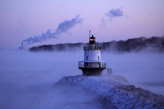 El faro Spring Point Ledge se destaca en medio de neblina proveniente del Ártico, y al fondo pueden verse las emisiones de la termoeléctrica Wyman arrastradas por los fuertes vientos, el sábado 4 de febrero de 2023, en South Portland, Maine. (AP Foto/Robert F. Bukaty)