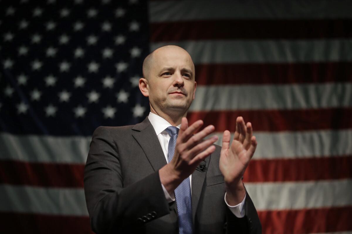 Evan McMullin claps while standing in front of a U.S. flag.