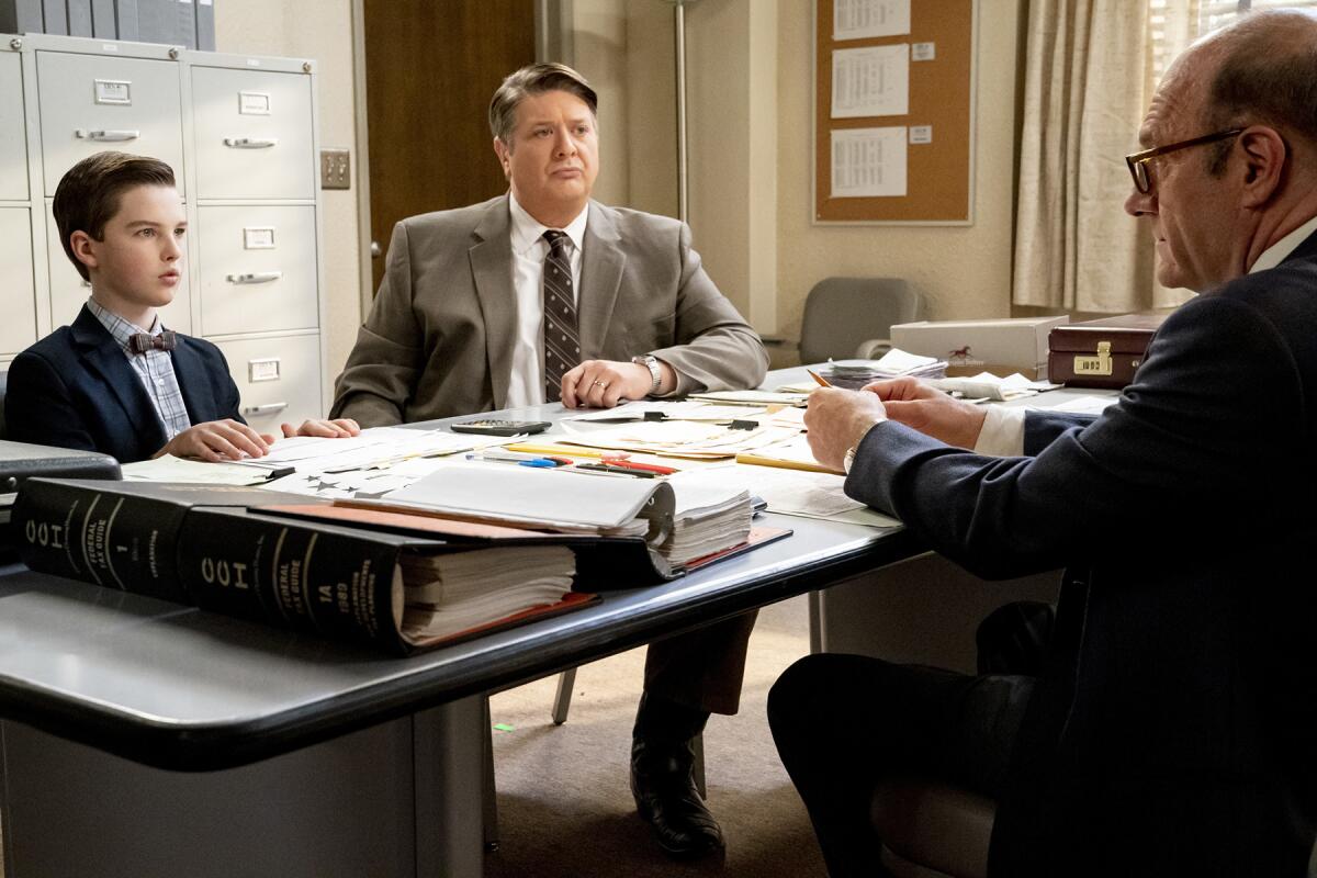 Iain Armitage, left, Lance Barber and Rob Brownstein sit at a table covered with papers.