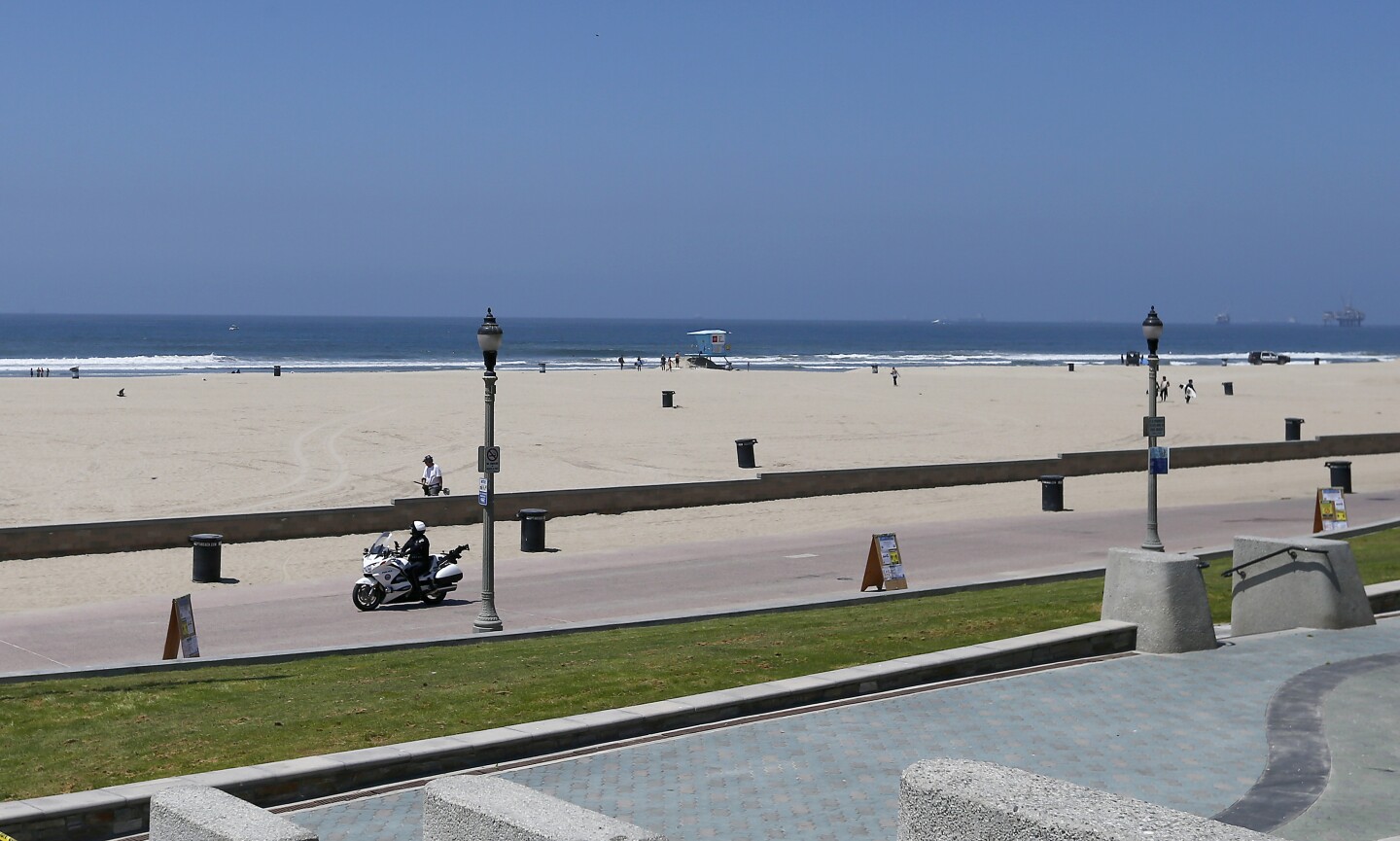 HUNTINGTON BEACH - MAY 2, 2020. A motorcycle cop patrols the bike path near the Huntington Beach Pier on Saturday, May 2, 2020. California Gov. Gavin Newson ordered a hard closure of Orange County beaches this weekend. But responding to public pressure in recent days, Newson has implied that a gradual reopening of beaches, parks and the economy following the coronavirus lockdown could begin as early as next week. (Luis Sinco/Los Angeles Times)