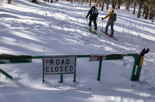 Two skiers pass a "Road Closed" sign on their trek up a backcountry slope.