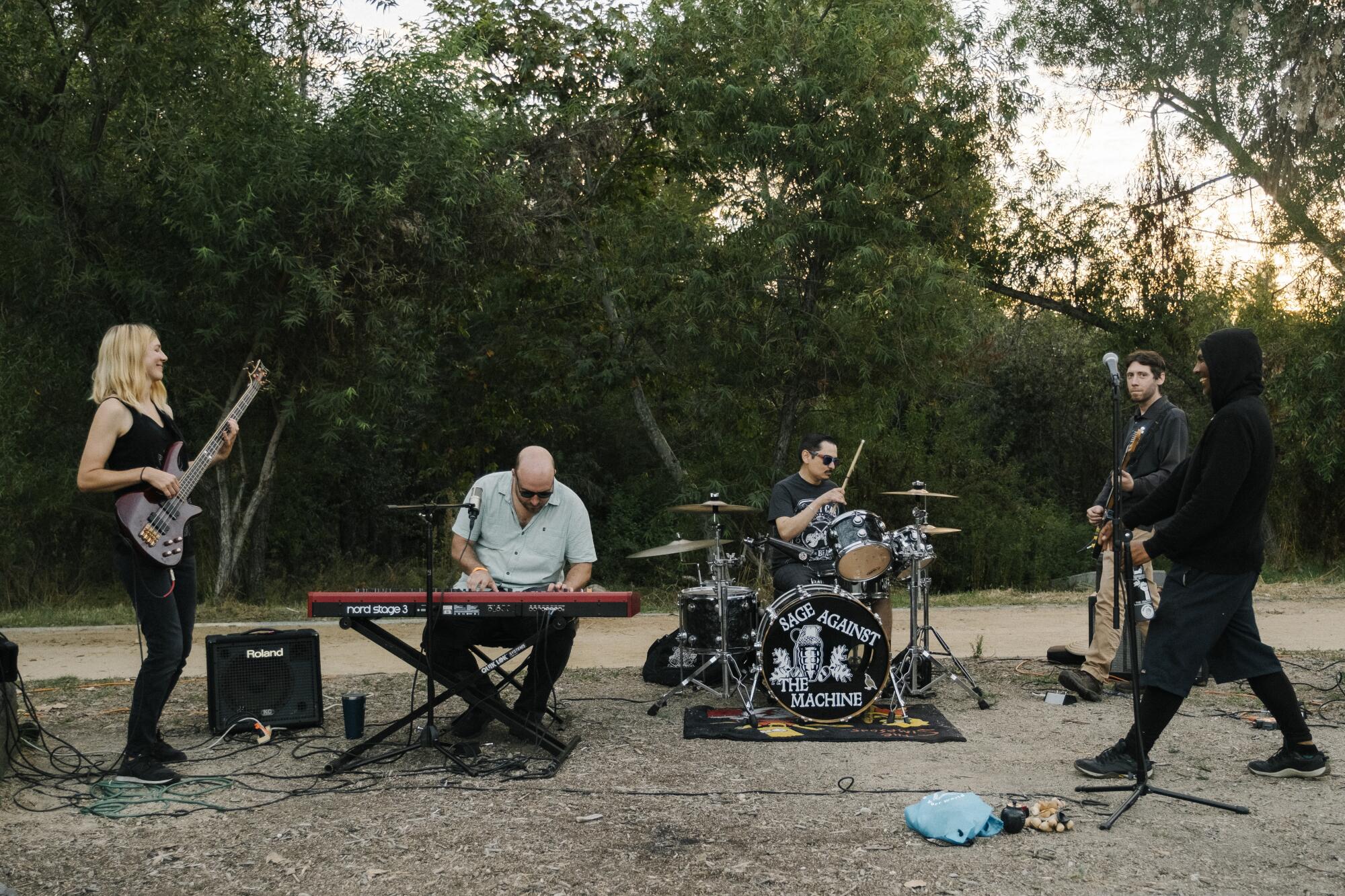 A rock band with five musicians playing bass, keyboards, drums and guitar outdoors.