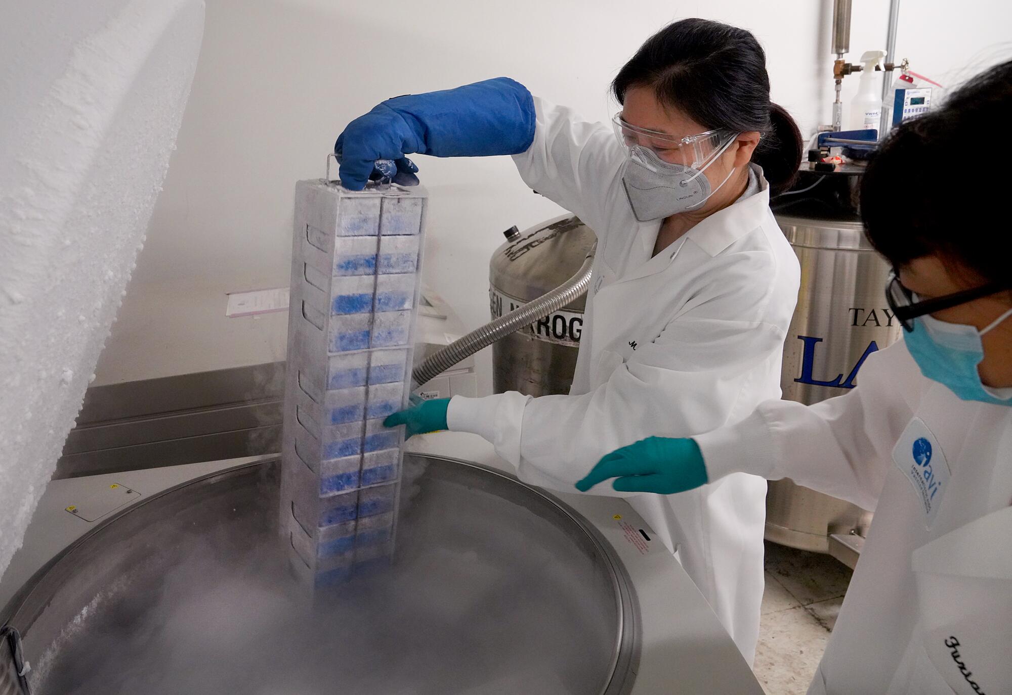 Two scientists pull virus samples from from cold storage.