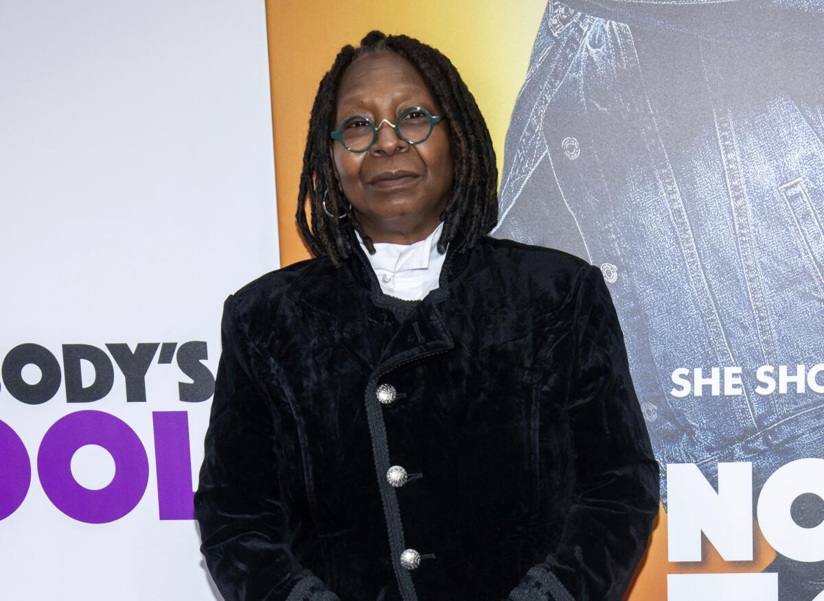 Whoopi Goldberg, in a black suit, poses at a red carpet event