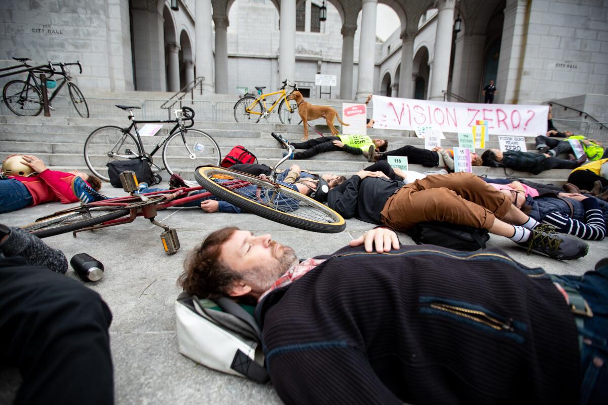 People lie on a sidewalk amid scattered bicycles as a dog stands near a banner reading "Vision Zero?"