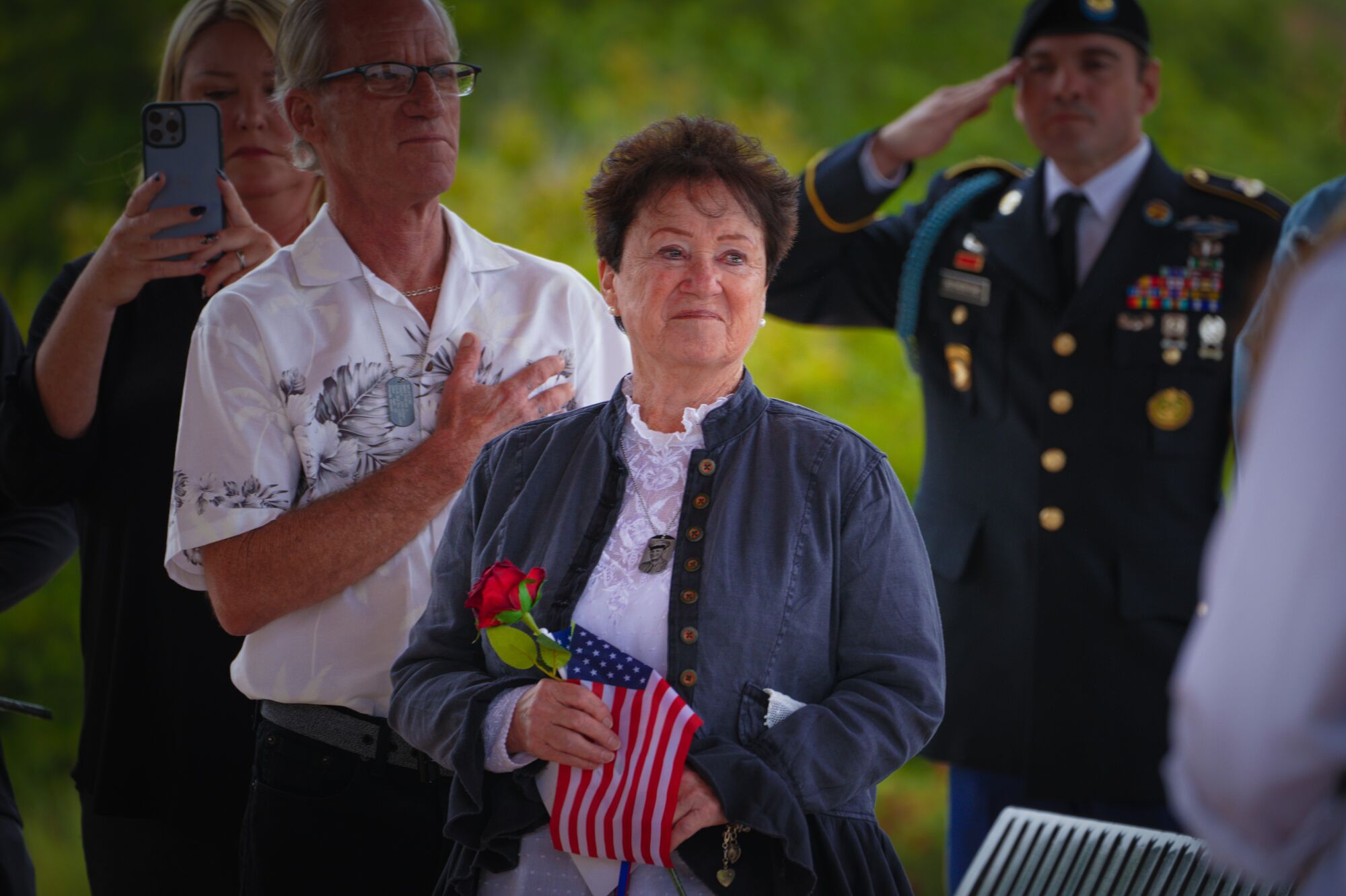 A woman holds a flower and a U.S. flag.