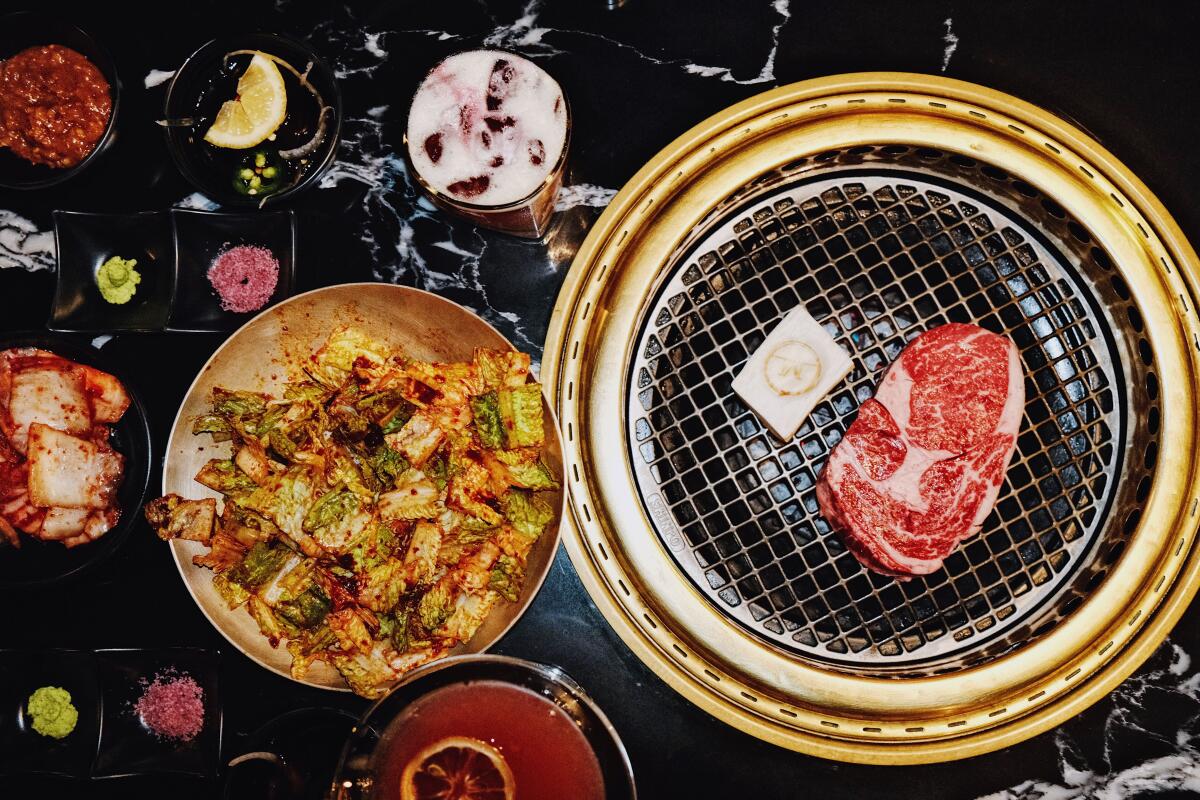 A steak on the grill at Mun Korean Steakhouse in Koreatown, with banchan, cocktails and salad also on the table.