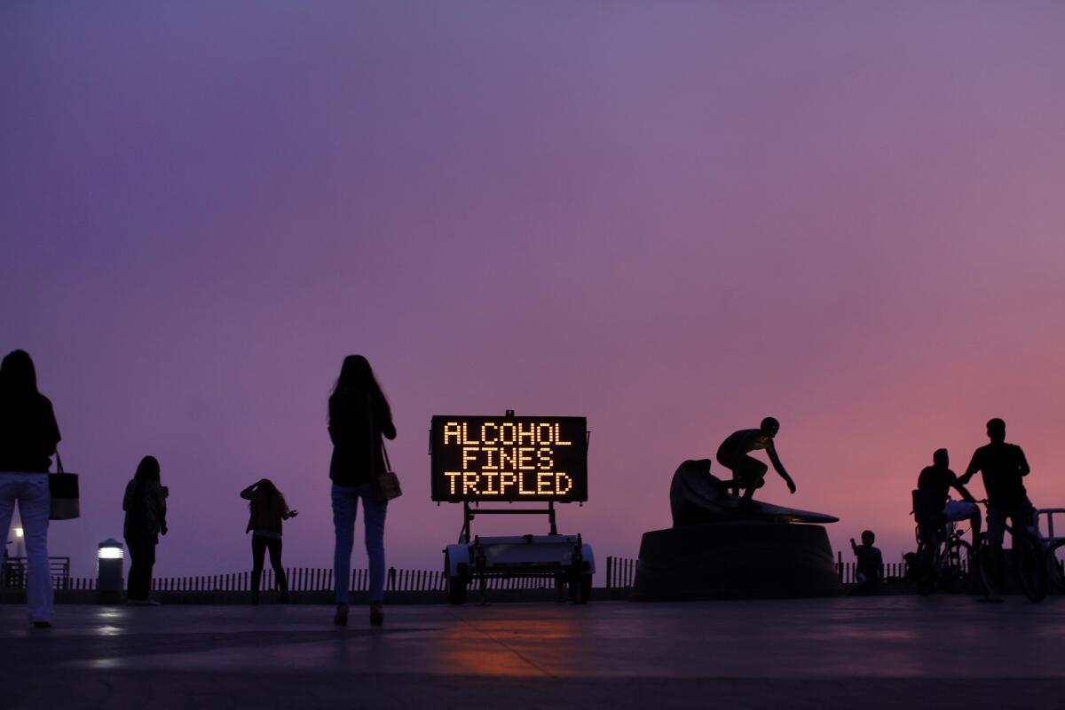 As the sun sets, a sign at the Hermosa Beach Pier reminds people that alcohol fines will be tripled during the holiday week.