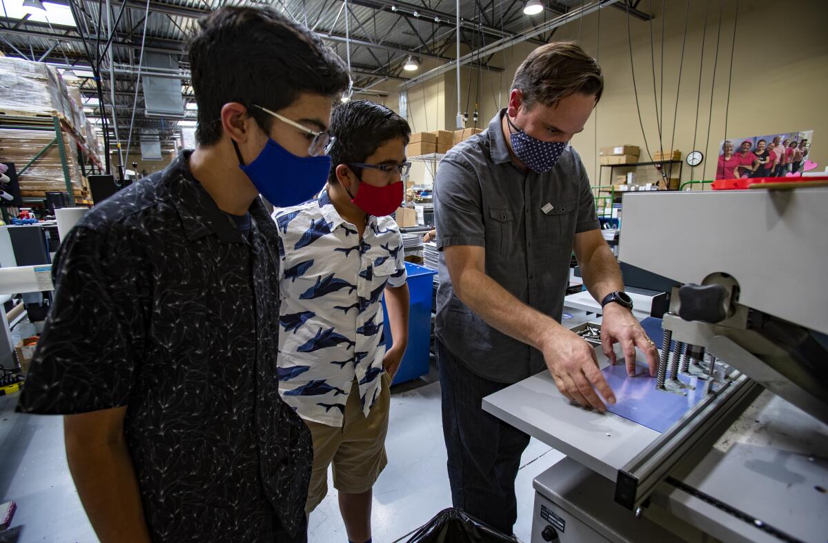 Zubin and Tenzing watch as warehouse director Andy McGuire makes holes in face shields so headbands can be attached.