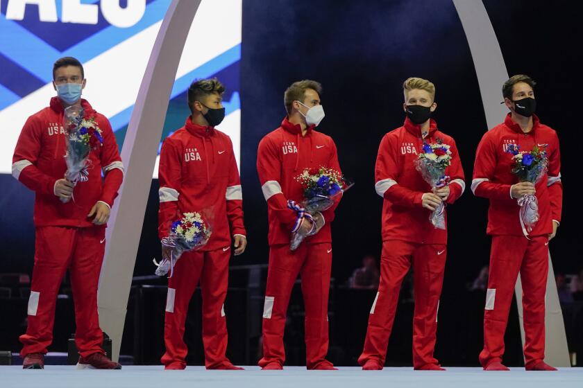 Members of the U.S. Men's Olympic Team wear masks and hold flowers while standing on stage