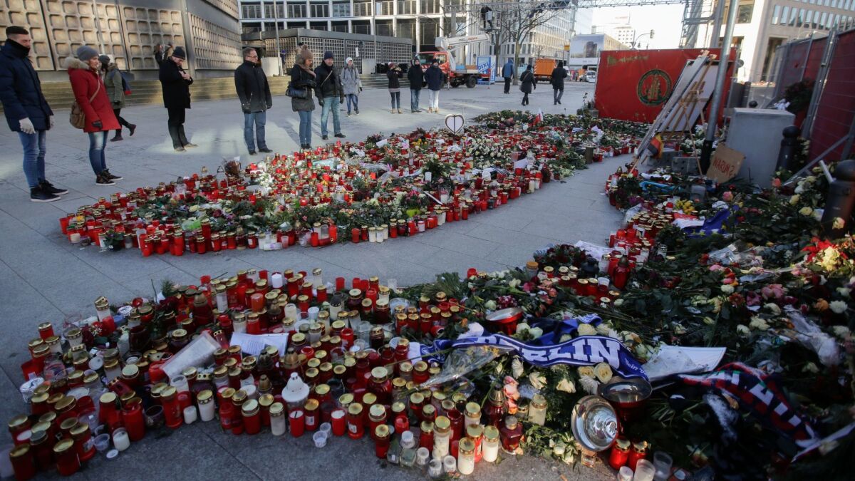People stand next to flowers and candles on Jan. 6, in memory of the victims of a truck attack in Berlin.