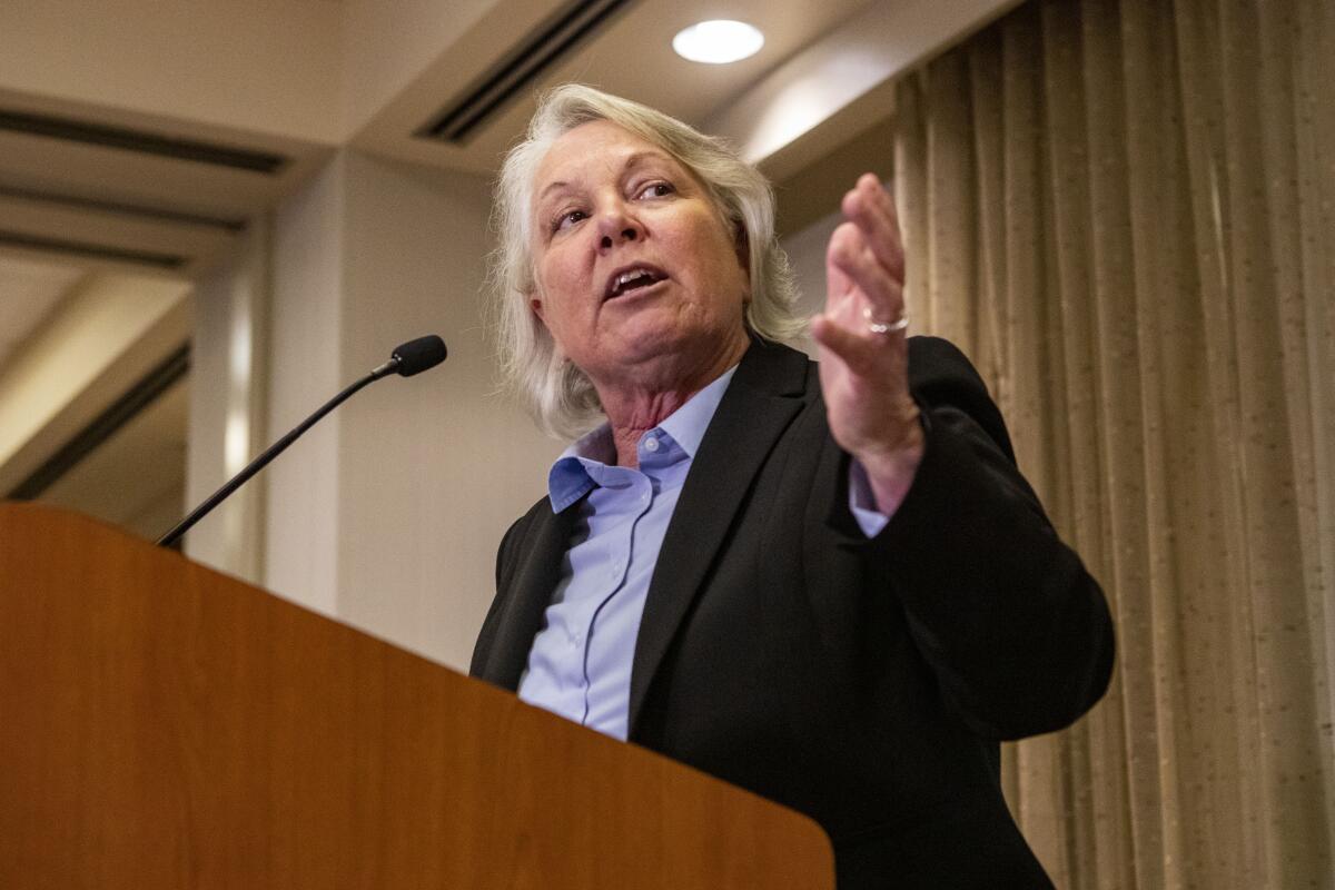 A woman wearing a blazer speaks at a podium