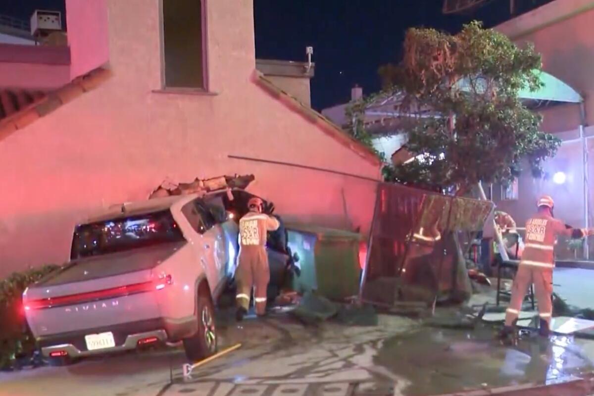 A Rivian truck is shown partially inside a store with emergency personnel outside it.