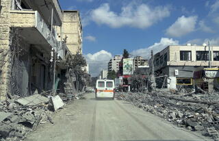 An ambulance drives down a road with the rubble of buildings on each side in Nabatieh, Lebanon.