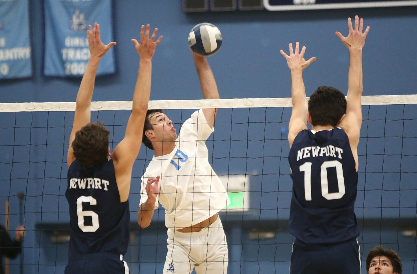 Corona del Mar's Nick Alacano (10) kills a ball between Newport Harbor blockers Blake Ludes and Caden Garrido (10) during second round of the Battle of the Bay boys' volleyball match in Surf League play on Wednesday.