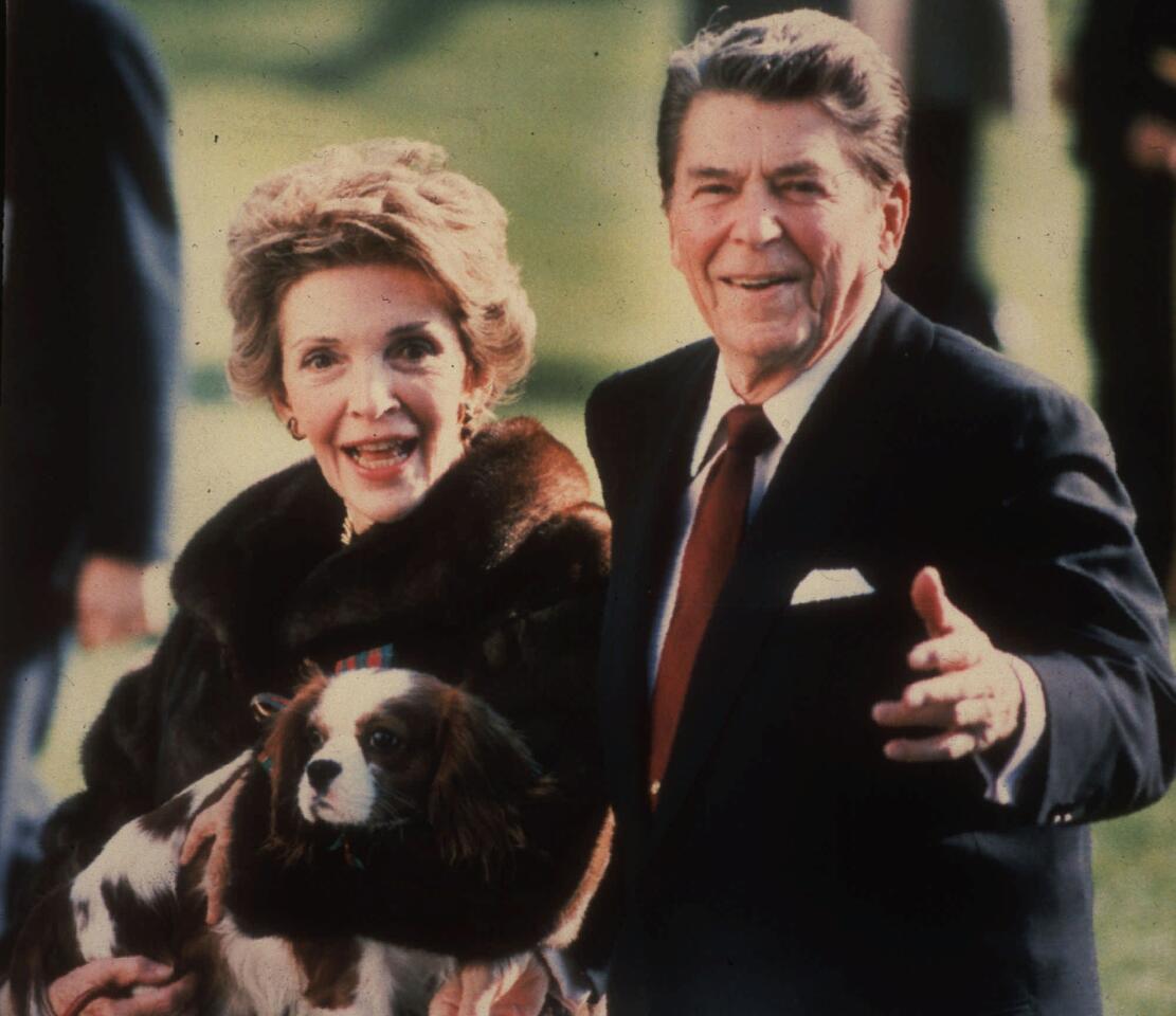 This December 1986, file photo shows first lady Nancy Reagan holding the Reagans' pet Rex, a King Charles spaniel, as she and President Reagan walk on the White House South lawn.