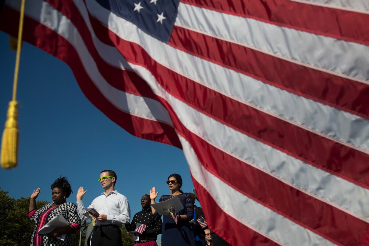 An American flag billows in the wind as immigrants stand and take the oath of allegiance.